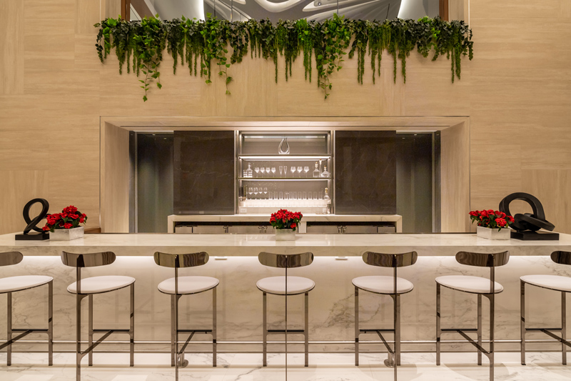 A glass bar fascia glows in the foreground of a marble tabletop and stools